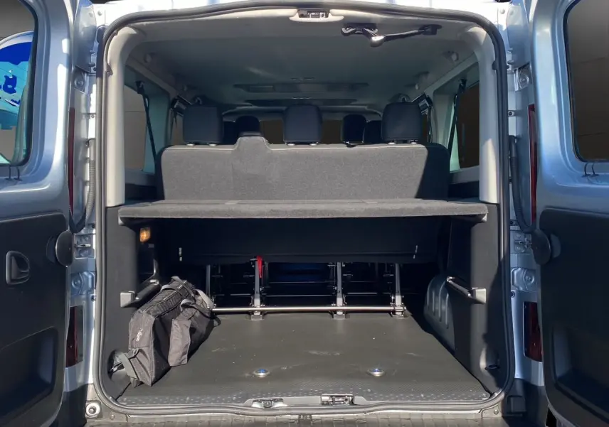 Vue arrière ouverte du Renault Trafic Combi gris Highland montrant le coffre spacieux avec banquette et sac noir.