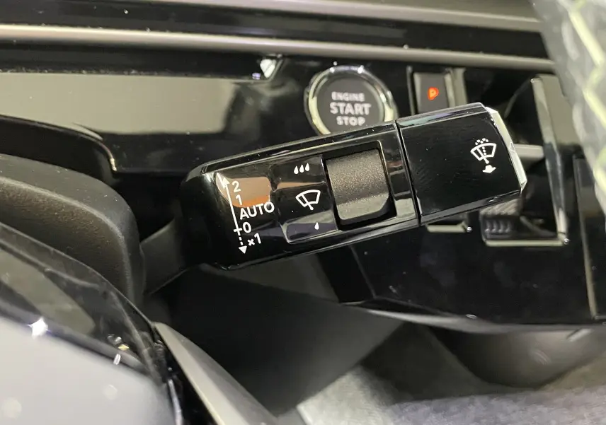 Gros plan sur la commande des essuie-glaces noire brillante du Peugeot 3008 Hybrid 2026 avec bouton Start/Stop en arrière-plan.