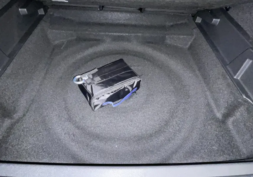 Vue plongeante sur le coffre vide d'un Peugeot 3008 Hybrid 2026, avec une petite trousse noire au centre.