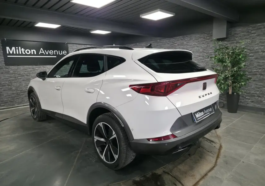 Vue 3/4 arrière droite du CUPRA Formentor blanc avec jantes alliage noires et bandeau lumineux arrière LED dans un showroom.