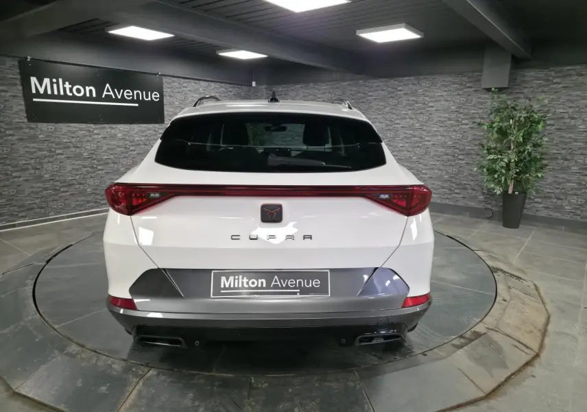 Vue arrière d'un CUPRA Formentor blanc avec bandeau lumineux rouge et double sortie d'échappement noire en intérieur showroom.