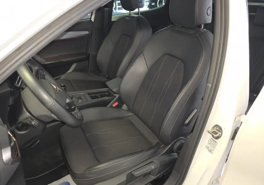 Vue intérieure côté conducteur du CUPRA Formentor blanc 2024, sièges sport noirs avec surpiqûres cuivre et volant multifonctions.