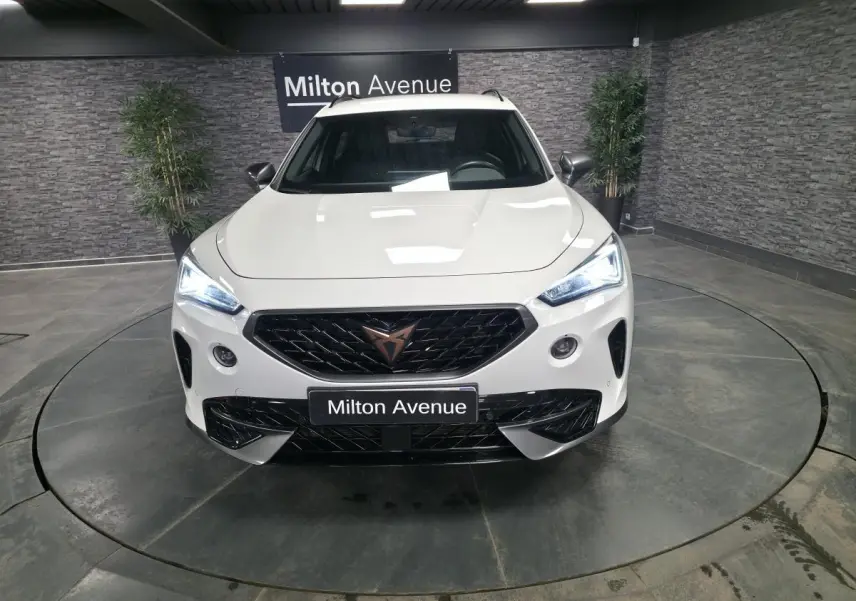 Vue frontale du CUPRA Formentor blanc avec calandre noire et feux LED allumés dans un showroom.