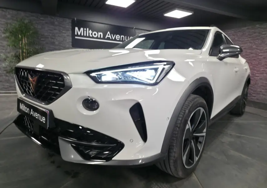 Vue 3/4 avant droit d'une CUPRA Formentor blanche avec calandre noire et phares LED allumés dans un showroom.