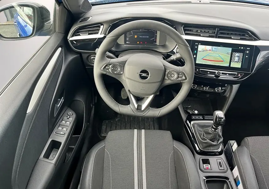 Vue intérieure avant centrée sur le volant sport et la console avec écran tactile, sièges noirs à surpiqûres grises.