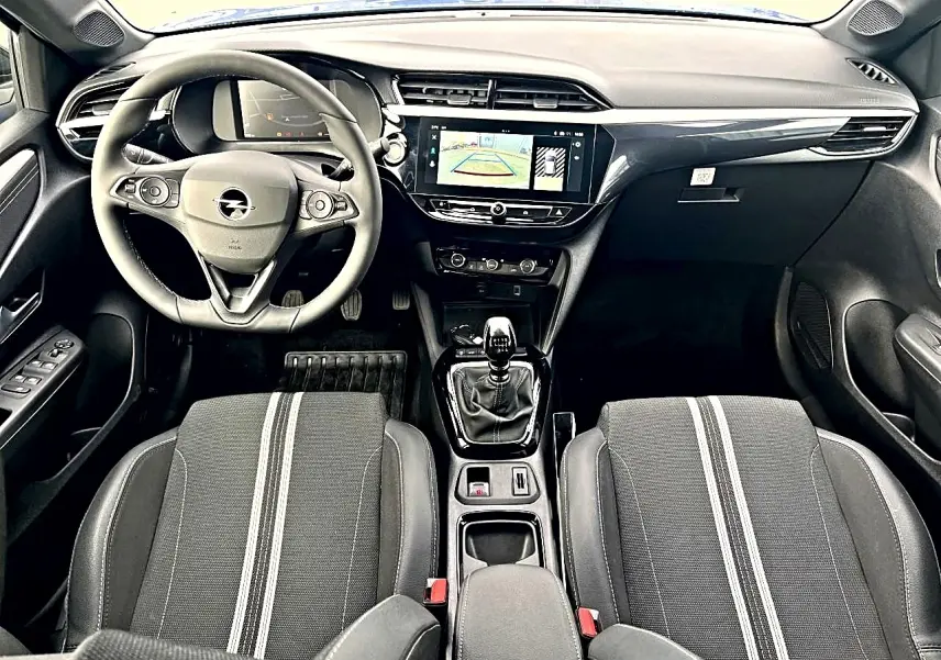 Vue intérieure avant de l’Opel Corsa 2025, tableau de bord noir avec écran tactile et sièges sport gris à bandes blanches.
