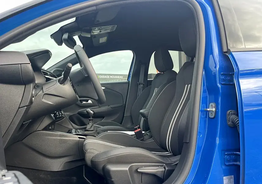 Vue intérieure côté conducteur d'une Opel Corsa bleu 2025, sièges sport noirs avec surpiqûres blanches et boîte manuelle.