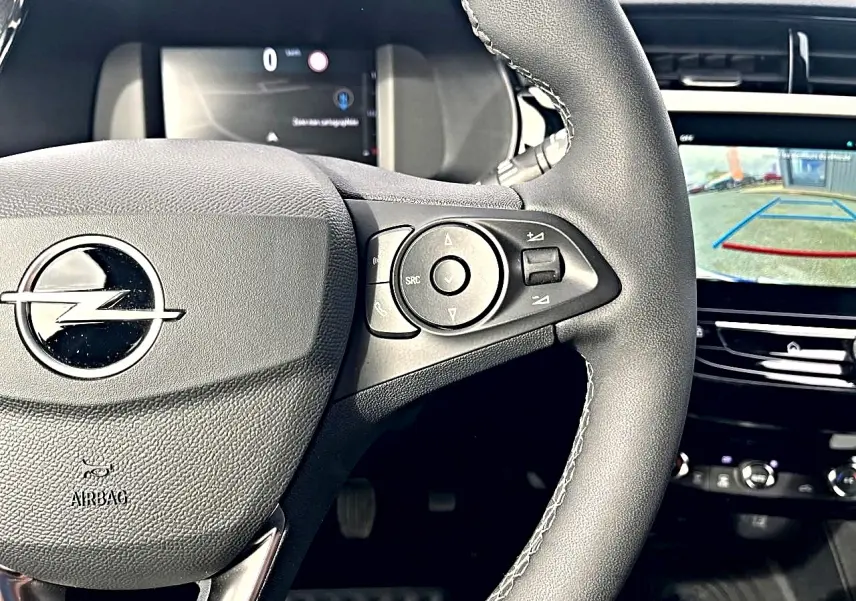 Gros plan sur le volant sport noir de l’Opel Corsa 2025 avec commandes multifonctions et écran tactile de caméra de recul.