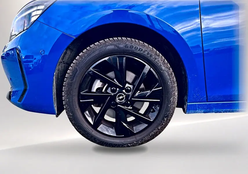 Gros plan sur la roue avant droite noire et jante alu d’une Opel Corsa bleu 2025, avec partie avant visible.