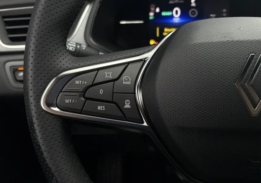 Gros plan sur le volant perforé noir du Renault Captur 2025 avec commandes de régulateur adaptatif et écran numérique en arrière-plan.