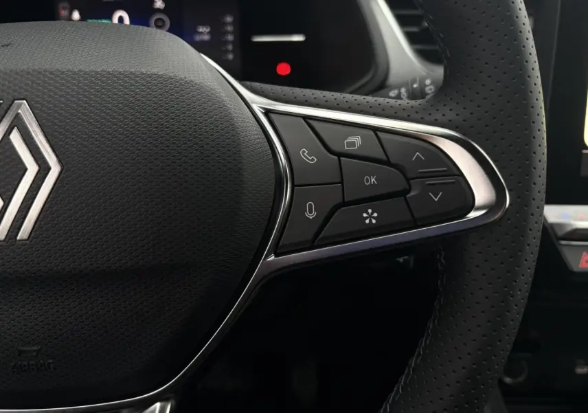 Gros plan sur le volant noir perforé du Renault Captur 2025, avec commandes multifonctions et logo Renault central argenté.