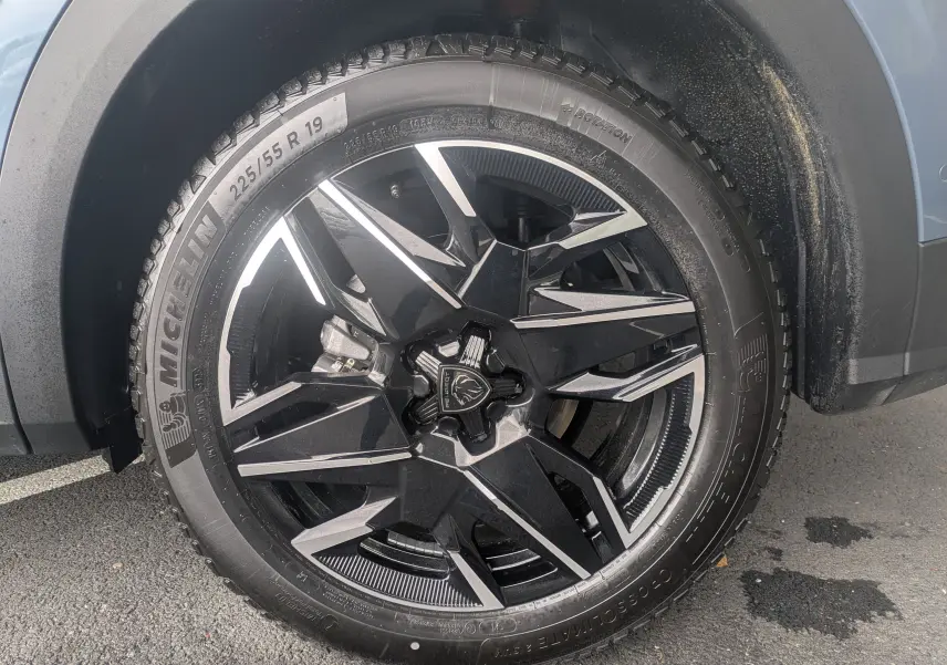 Gros plan sur la jante alliage 19'' noire et argent du Peugeot 3008 Hybrid 145 bleu Ingaro, avec pneu Michelin.