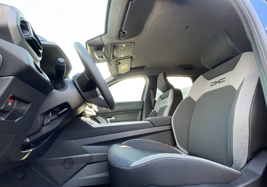 Intérieur du Dacia Bigster Hybrid 155 Journey City, vue côté conducteur, sièges bi-matière gris et noir avec logo DC.