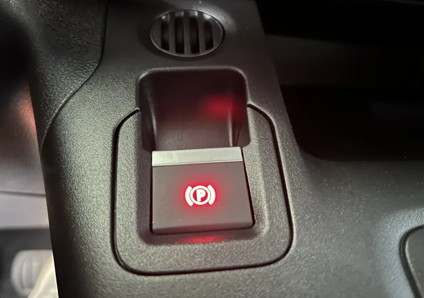 Gros plan sur le bouton de frein à main électrique rouge dans l'habitacle du Citroën Berlingo Multispace gris acier.