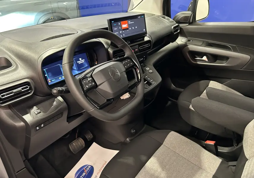Vue intérieure côté conducteur du Citroën Berlingo Multispace 2026, volant cuir, tableau de bord digital et sièges tissu gris et noir.