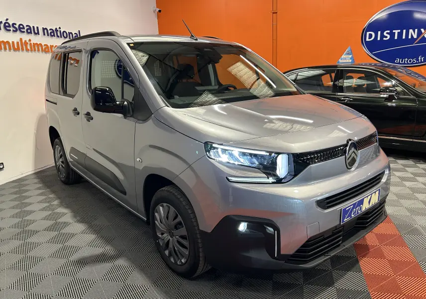 Vue 3/4 avant droit du Citroën Berlingo Multispace gris acier avec phares allumés en intérieur showroom.