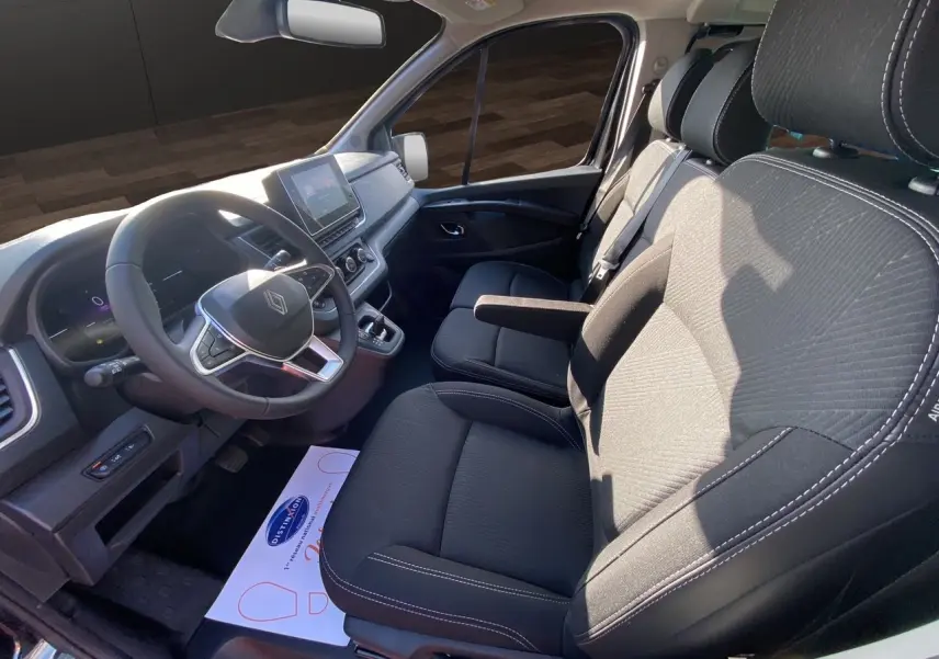 Intérieur avant du Renault Trafic Combi noir 2025, sièges tissu noir et tableau de bord avec écran tactile central.