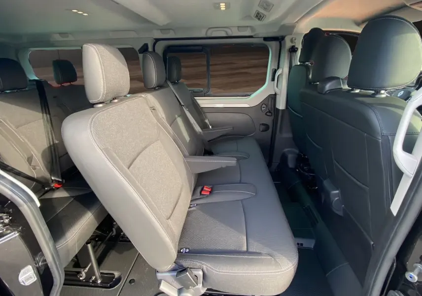 Intérieur du Renault Trafic Combi 2025 vu côté gauche, banquettes tissu noir avec accoudoirs et ceintures de sécurité.