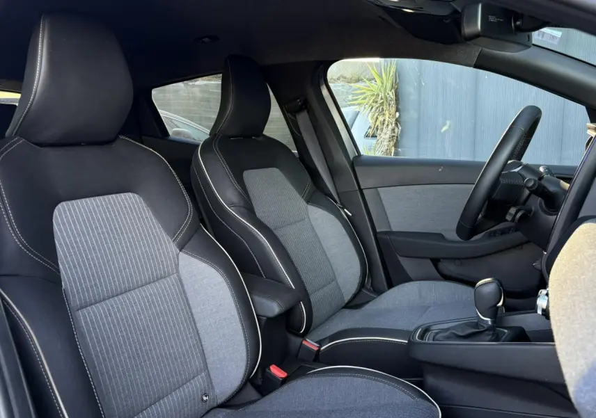 Vue intérieure côté droit de la Renault Clio 2025, sièges bi-matière gris et noir avec surpiqûres blanches.