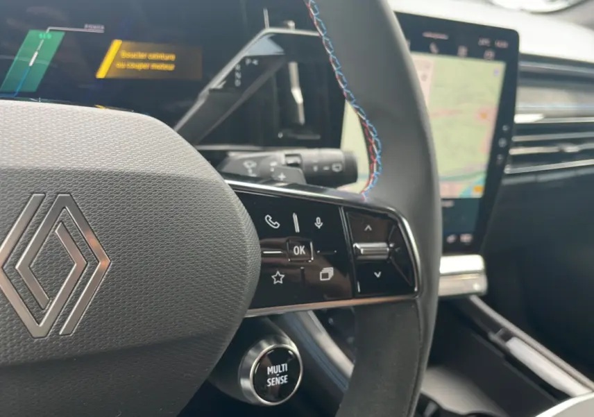 Gros plan sur le volant multifonctions avec surpiqûres bleues et écran tactile du tableau de bord du Renault Austral gris schiste.