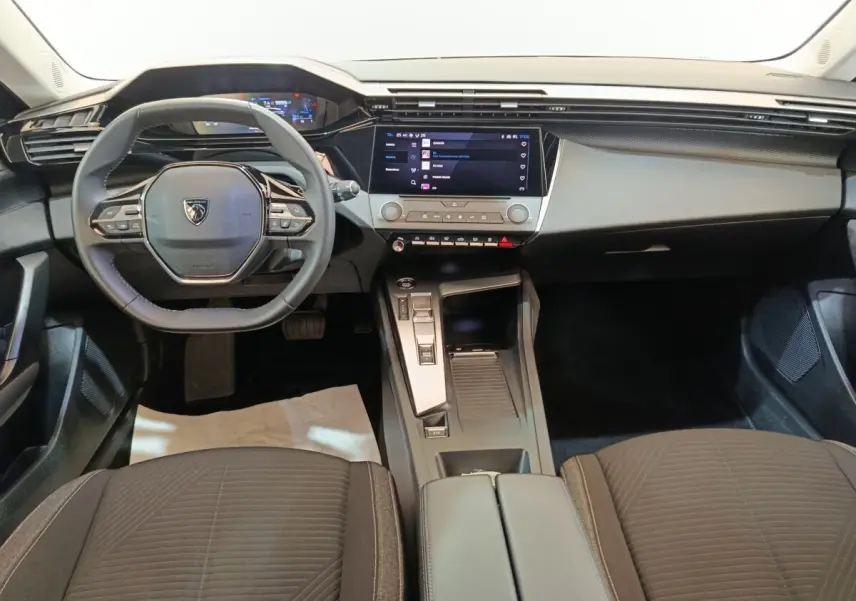 Vue intérieure avant centrée du tableau de bord et volant cuir noir de la Peugeot 308 2022 PureTech blanche.