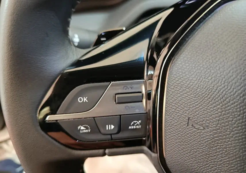 Gros plan sur les commandes multifonctions noires à gauche du volant cuir d’une Peugeot 308 blanche.