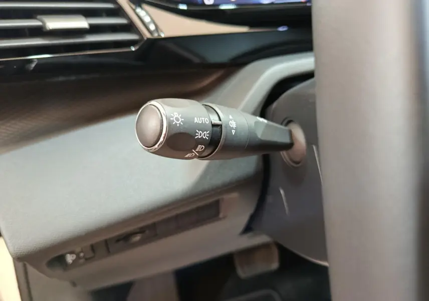 Gros plan sur la commande des feux à gauche du volant dans l’habitacle sombre d’une Peugeot 308 blanche.
