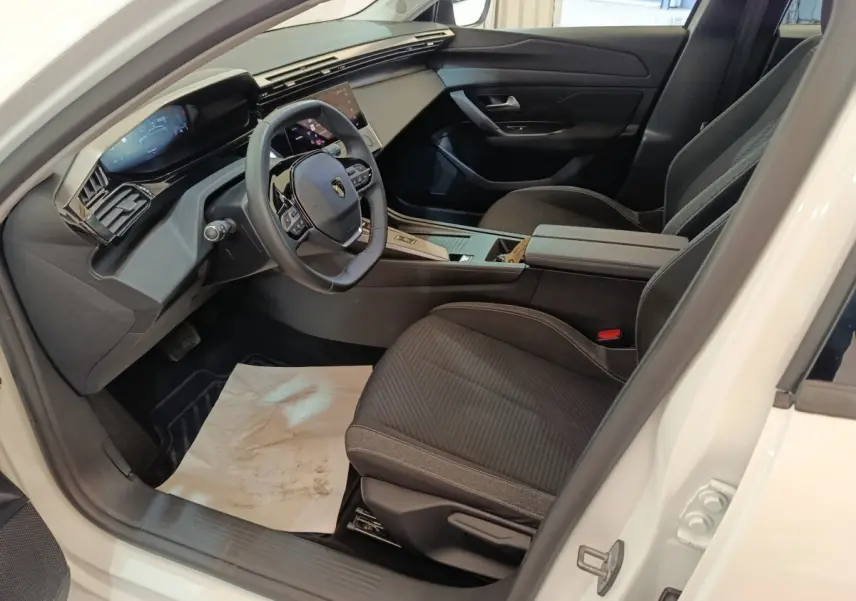 Intérieur avant droit de la Peugeot 308 blanche 2022, avec tableau de bord digital et sièges tissu noirs.