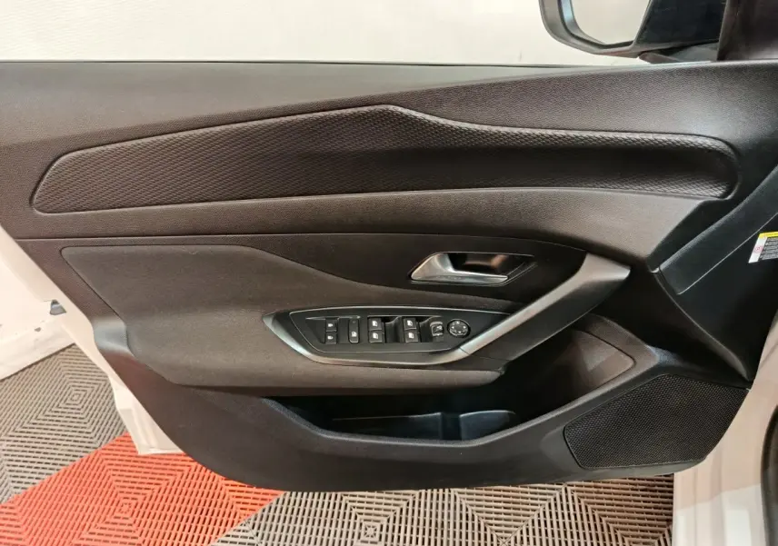 Vue rapprochée de la porte avant gauche noire de la Peugeot 308 blanche avec commandes électriques des vitres et rétroviseurs.