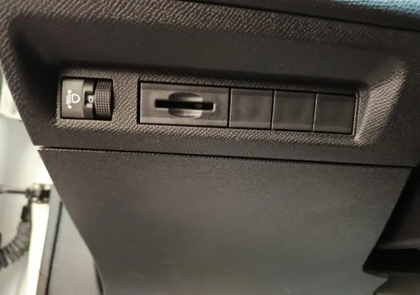 Détail intérieur côté conducteur de la Peugeot 308 blanche 2022 montrant les commandes de réglage des phares.