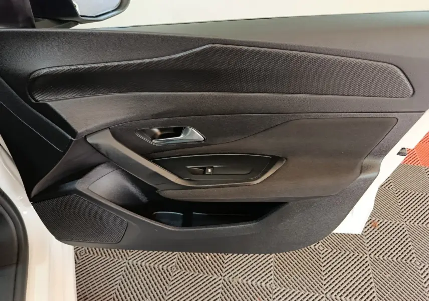 Vue rapprochée de la porte avant gauche noire d’une Peugeot 308 blanche, mettant en valeur la poignée et les commandes de fenêtre.
