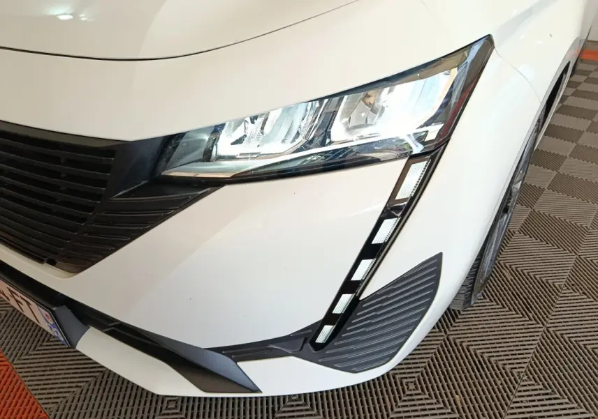 Gros plan sur l'avant droit blanc de la Peugeot 308 2022 avec phares LED et calandre noire distinctive.