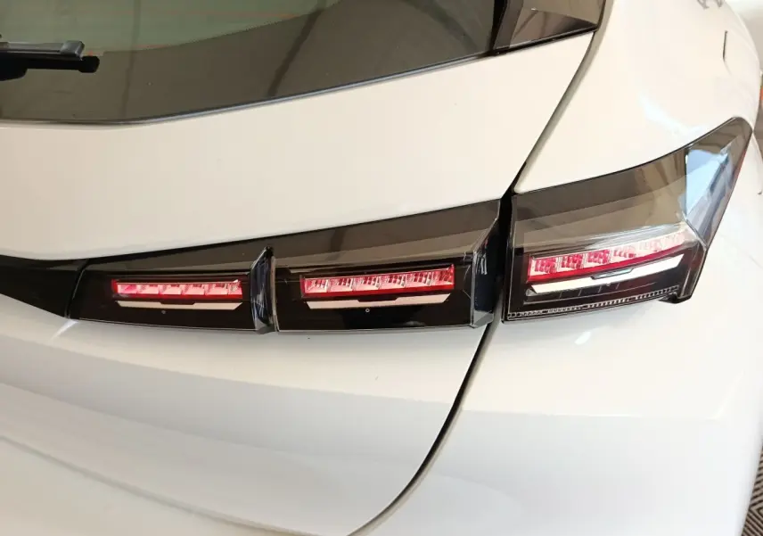 Gros plan sur les feux arrière rouges et noirs d'une Peugeot 308 blanche vue de l'arrière droit.