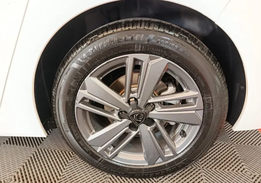 Gros plan sur la roue avant droite d'une Peugeot 308 blanche, jante alliage gris avec logo Lion central.