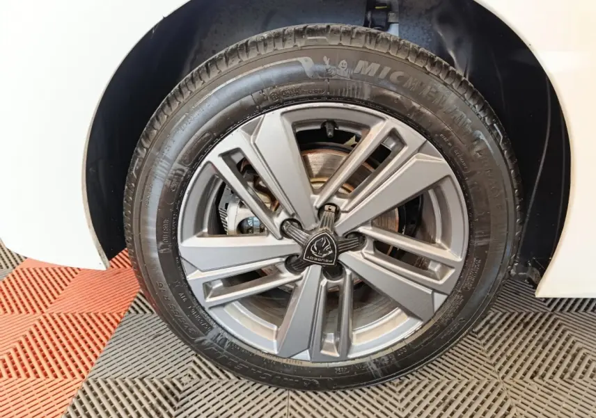 Gros plan sur la roue avant droite de la Peugeot 308 blanche, mettant en valeur la jante alliage grise au design moderne.