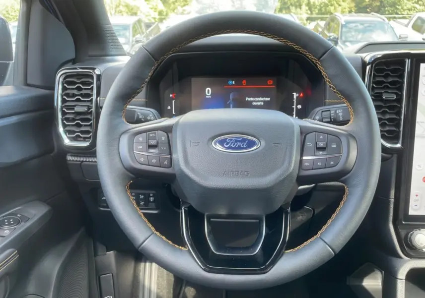 Vue rapprochée du volant cuir noir avec surpiqûres orange du Ford Ranger 2025, tableau de bord et écran tactile visibles.