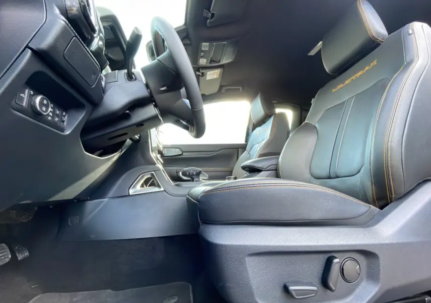 Vue intérieure côté conducteur du Ford Ranger Wildtrak 2025, sièges cuir noirs avec surpiqûres orange et logo Wildtrak brodé.
