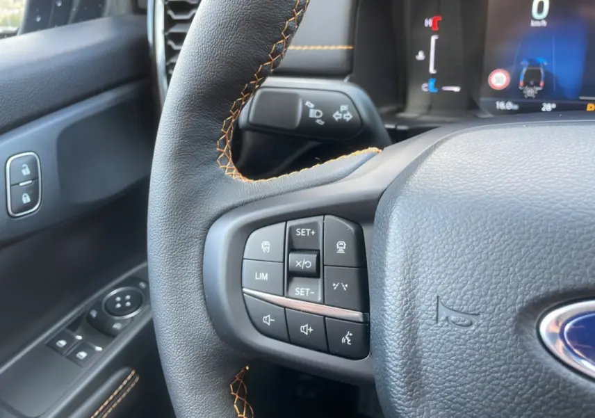 Gros plan sur le volant cuir noir avec surpiqûres orange et commandes multifonctions du Ford Ranger Wildtrak 2025.
