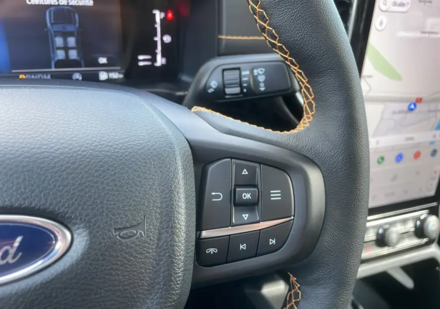 Gros plan sur le volant cuir noir avec surpiqûres orange du Ford Ranger 2025, affichage numérique et écran tactile visible.