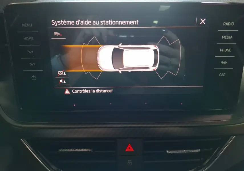 Écran central du Skoda Kamiq blanc montrant l'aide au stationnement avec alertes de distance active.