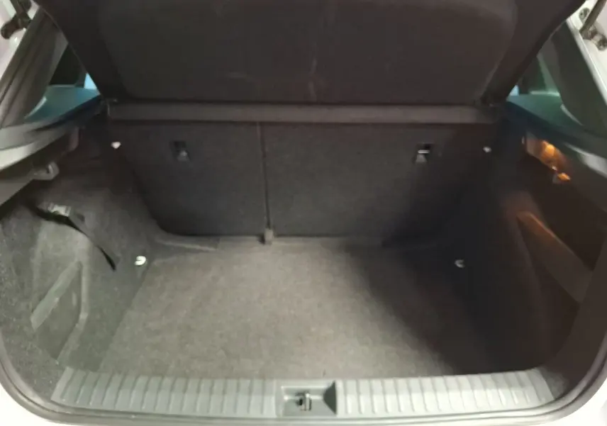 Coffre ouvert d’un Skoda Kamiq blanc, vue de l’arrière montrant l’espace de chargement vide et tapis gris.