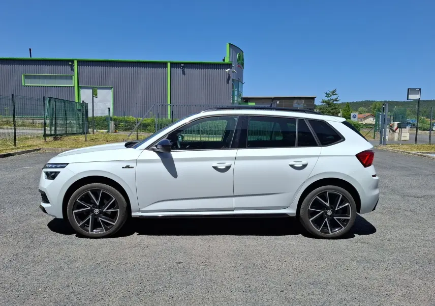 Vue de profil côté gauche d’un Skoda Kamiq blanc 2021 avec jantes alliage noires et toit panoramique visible.