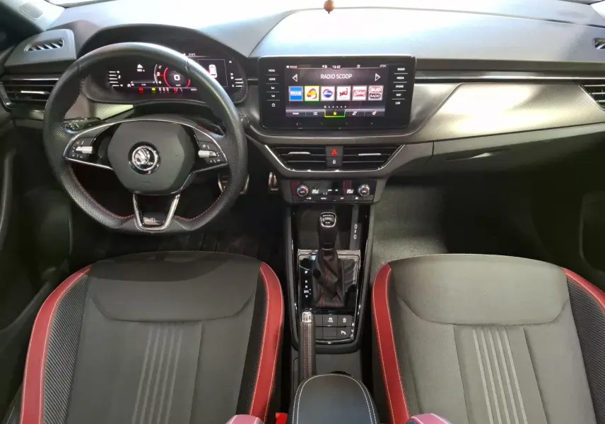 Vue intérieure frontale du Skoda Kamiq 1.0 TSI 110 Monte Carlo avec volant sport, écran tactile et sièges noirs à surpiqûres rouges.