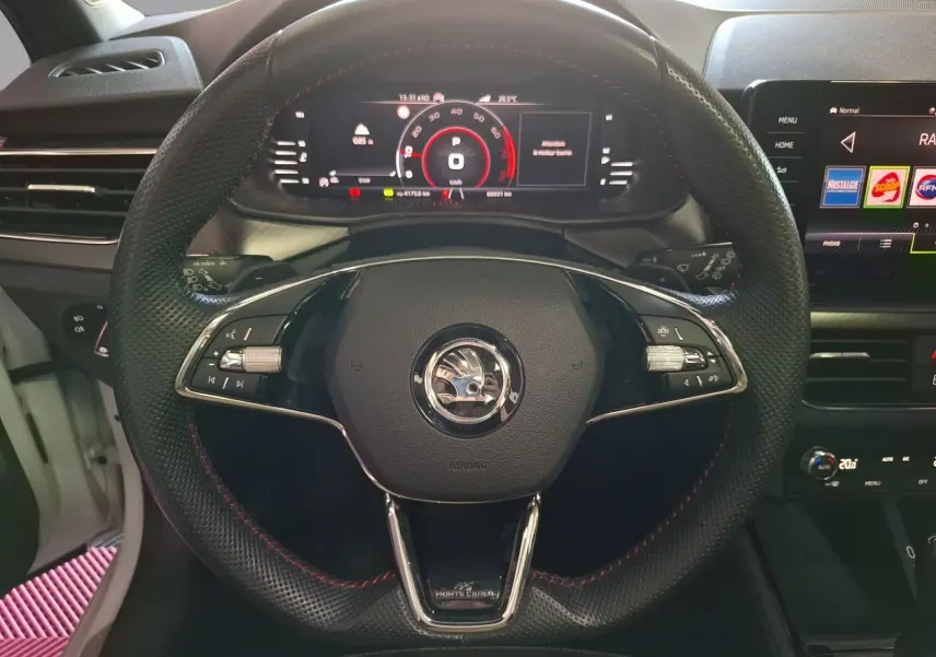 Vue centrée du volant noir perforé avec surpiqûres rouges d'une Skoda Kamiq Monte Carlo 2021, tableau de bord numérique allumé.