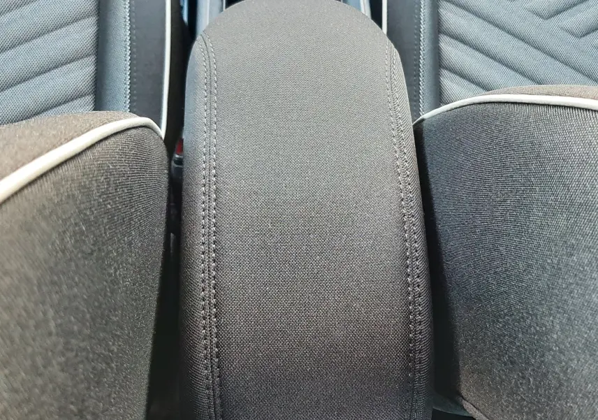 Détail de l'accoudoir central en tissu gris entre les sièges avant du Fiat 600 vert Sky 2025.