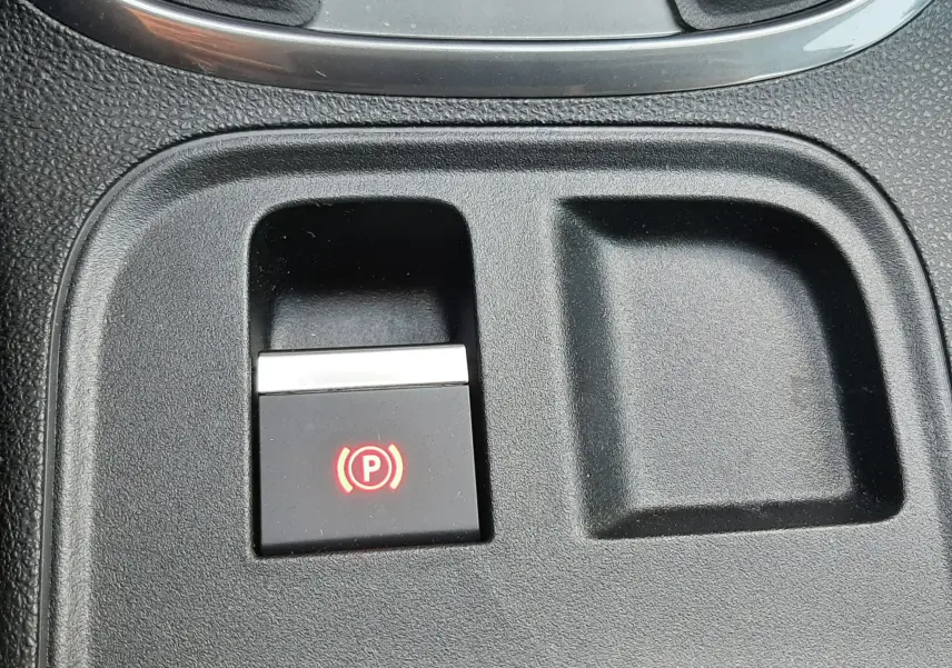 Gros plan sur le bouton de frein à main électronique rouge dans la console centrale d'une FIAT 600 1.2 Hybrid 2025 vert Sky.