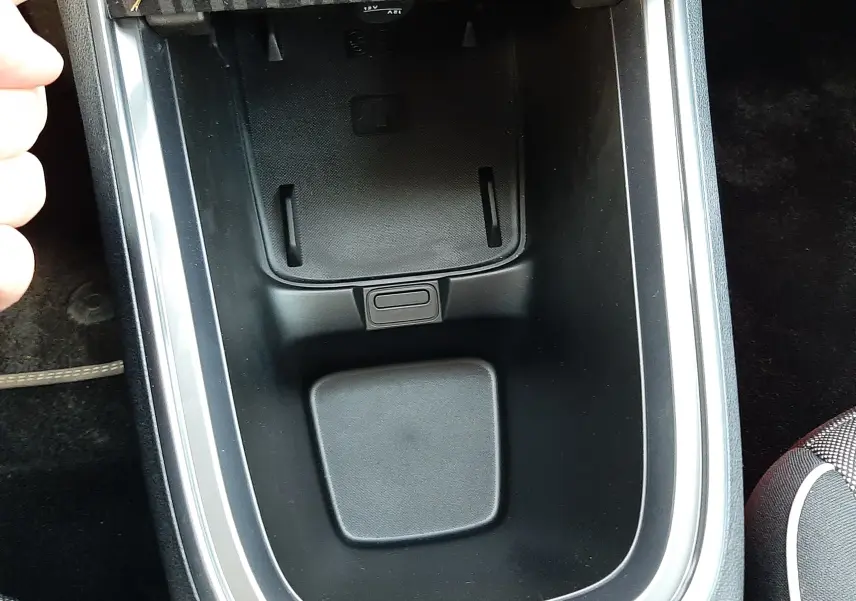 Vue rapprochée de la console centrale noire avec un compartiment de rangement et un cache FIAT dans une Fiat 600 hybride 2025.