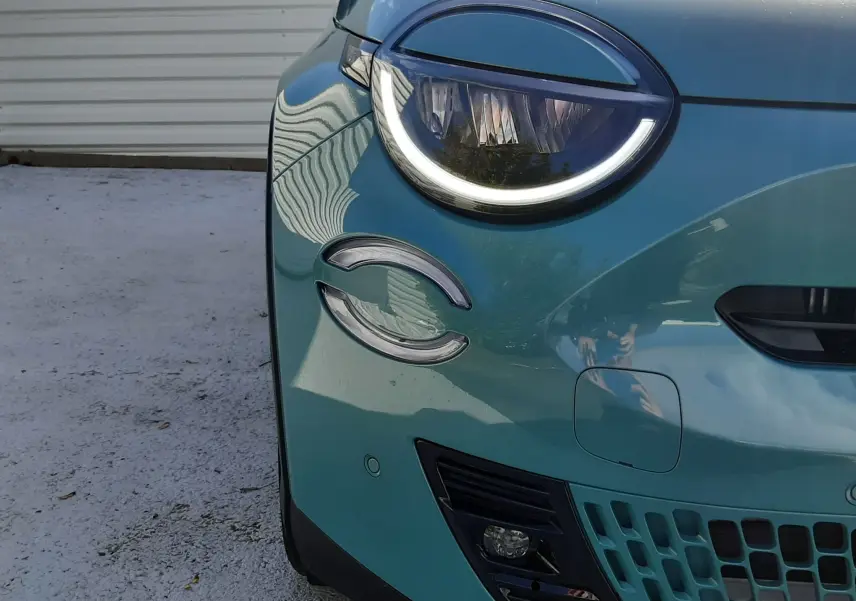 Gros plan sur l'avant gauche d'une FIAT 600 1.2 Hybrid 2025 en vert sky, mettant en valeur son phare rond à LED et sa calandre ajourée.