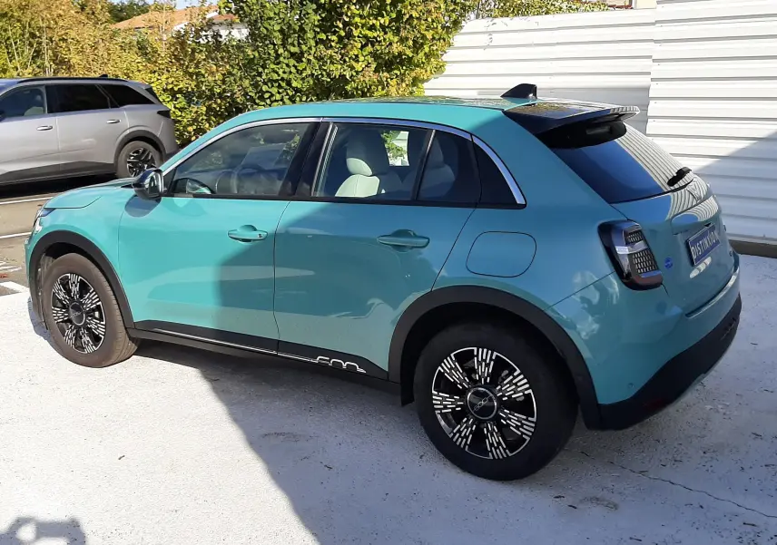 Vue de côté droit arrière d'une FIAT 600 1.2 Hybrid 2025 en vert sky avec jantes noires à motifs blancs et toit noir.