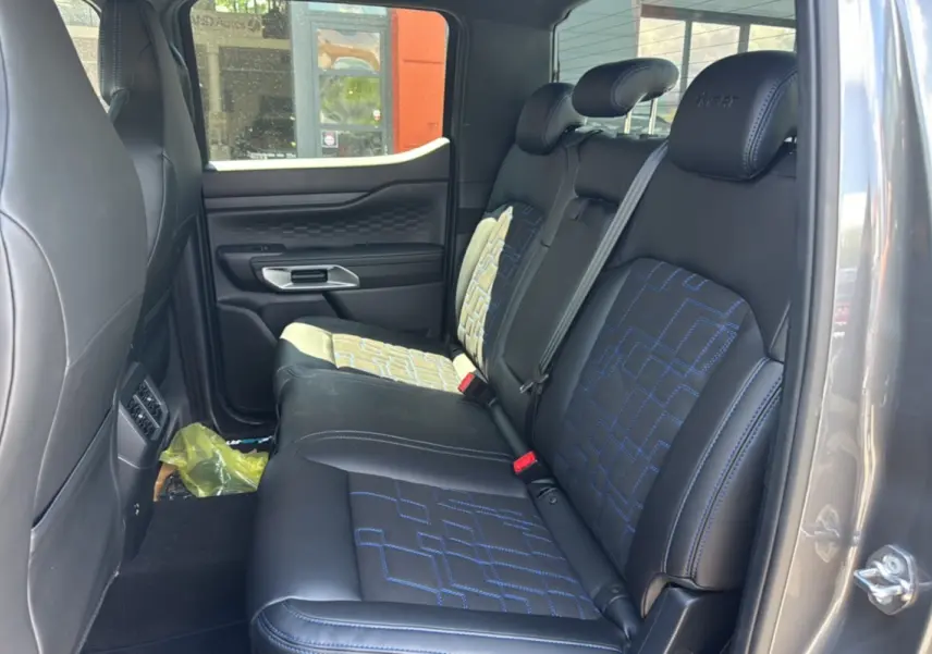 Vue intérieure côté arrière droit du Ford Ranger 3.0 V6 gris carbone, montrant les sièges arrière en cuir noir avec surpiqûres bleues.